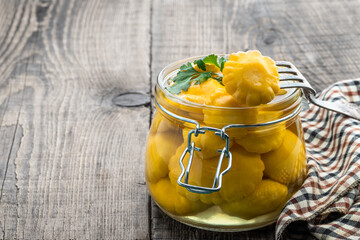 Marinated yellow squash in glass jar on wooden table