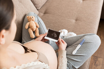 Pregnant Woman sitting on bed and Looking At Ultrasound Scan photo of her Baby. A pregnant female...