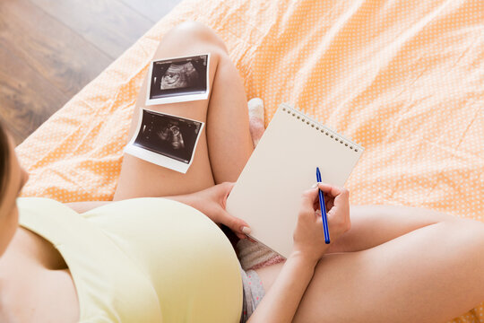 Top view caring future mother writing diary with ultrasound. pregnant woman tummy making notes feeling during pregnancy or creating scrapbook