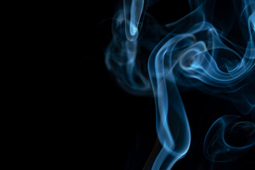 White blue cloud of smoke from smoking a cigar on an isolated black background. Fumes from smolder cigarette floating in the space. Smoke flying in the air and illuminated by light. Macro shot.