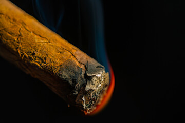 Smoking cuban cigar with blue smoke on an isolated black background. A Havana cigar burns and emits...