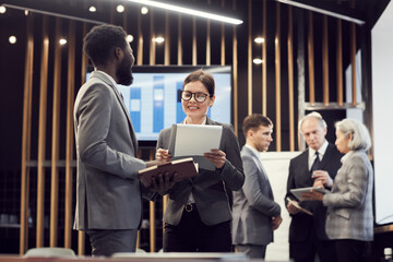 Positive multi-ethnic business colleagues in formalwear standing in meeting room and researching...