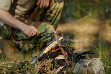 Man in military clothes is making campfire in the woods. The concept of adventure, travel, tourism, camping, survival and evacuation.