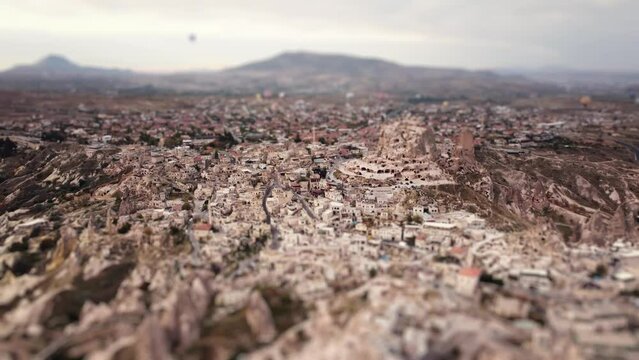 Aerial view on Uchisar castle and ancient city filmed by drone with tilt shift effect. Landscape of a town in sandstone rocks and flying hot air balloons on the background. Popular travel destinations