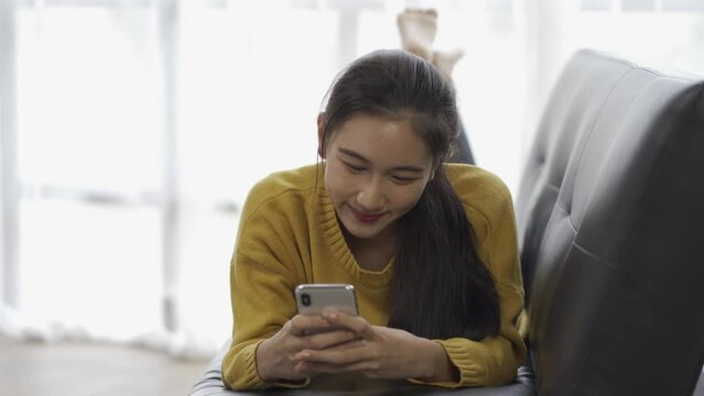 Asian woman enjoys playing on the phone, and chatting with friends on the Internet on a sofa at home.
