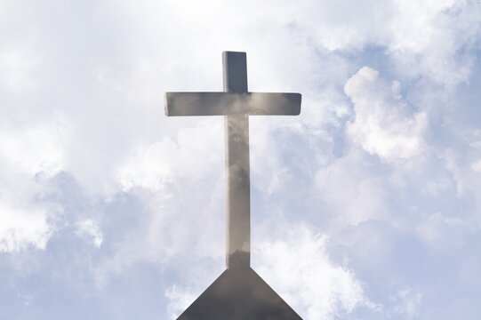 Silhouette of Christian cross over clouds against sky in the background. Easter religion faith concept