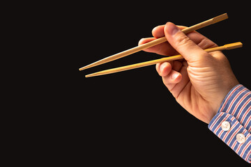 bamboo chopsticks in a male hand on a dark background. items for food