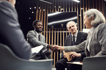 Positive handsome young Afro-American businessman sitting in circle of like-minded people and...