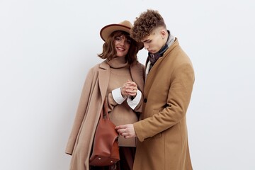 a beautiful couple in love is standing on a white background in autumn clothes and holding hands sweetly, a woman has an autumn hat on her head and a bag in her hand