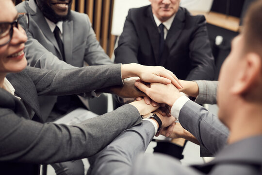 Close-up of solid team of business professionals standing in circle and stacking hands as symbol of unity at training class for business company