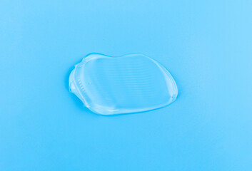 Smear of cosmetology transparent product for face treatment. Drop of cream on blue background. Lotion or mask. Beauty wellness and professional skincare concept.