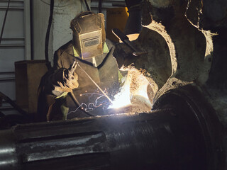 welder in protective mask and uniform repairs a large part
