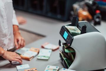 Bank employees using money counting machine while sorting and counting paper banknotes inside bank vault. Large amounts of money in the bank
