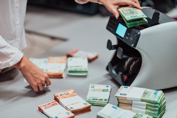 Bank employees using money counting machine while sorting and counting paper banknotes inside bank vault. Large amounts of money in the bank