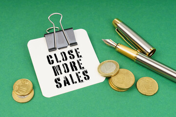 On a green surface, a pen, coins and a notepad with the inscription - Close More Sales