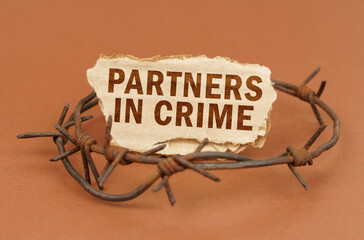 On a brown surface, barbed wire and a cardboard sign with the inscription - Partners in Crime