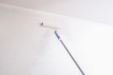 A man is painting vinyl wallpaper with a velour roller for painting with white paint. Renovation of the room.