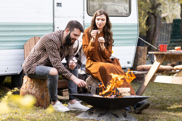 Young beautiful loving couple travelling across country in the van. Millennial man and woman in a travel camper. Cozy atmosphere, vacations vibe. Playing guitar, drinking tea, cooking on a campfire