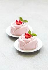 Vegan dessert. Strawberry cream pudding, Panna Cotta, in the shape of a rose, on a plate. Light grey background