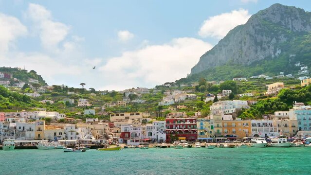 View of the Tyrrhenian sea coast in Capri, Italy. Classic buildings, piers with moored boats, greenery. View from a ship. Slow motion