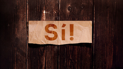 "Sí" Message for card, presentation and work. Rustic design on wooden background with kraft paper cut out. Can be used for business, marketing and advertising.