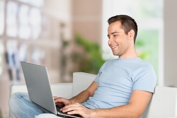 Portrait of smiling man using laptop. Adult male sitting on comfy couch in living room, watching video, taking break