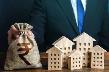 A businessman puts a indian rupee money bag near the houses. Investments in real estate assets....