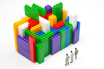 Obraz premium miniature people. figures of people stand near the colored blocks of a plastic constructor on a white background in the form of multi-storey buildings. concept of modern buildings and houses