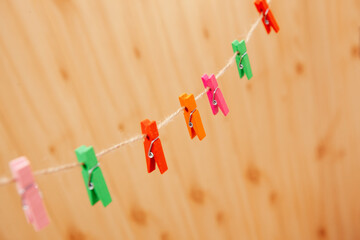 Different colors clothespins on rope with wooden backdrop, abstract background