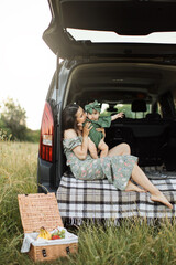Mother and daughter together at a picnic in thr car trunk. Toddler girl and young mother playing, spend time together. Walk outdoors in summer. Carelessness is a game of motherhood.