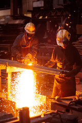 Two workers in a factory cutting a steel plate with a acetylene torch