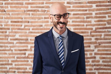 Bald man with beard wearing business clothes and glasses winking looking at the camera with sexy...