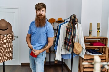 Young redhead robber man stealing shirt at clothes store.
