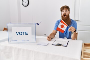 Caucasian man with long beard at political campaign election holding canada flag scared and amazed with open mouth for surprise, disbelief face