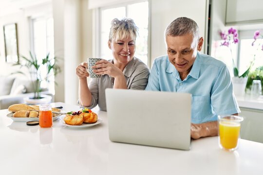 Senior caucasian couple having breakfast using laptop at the kitchen.