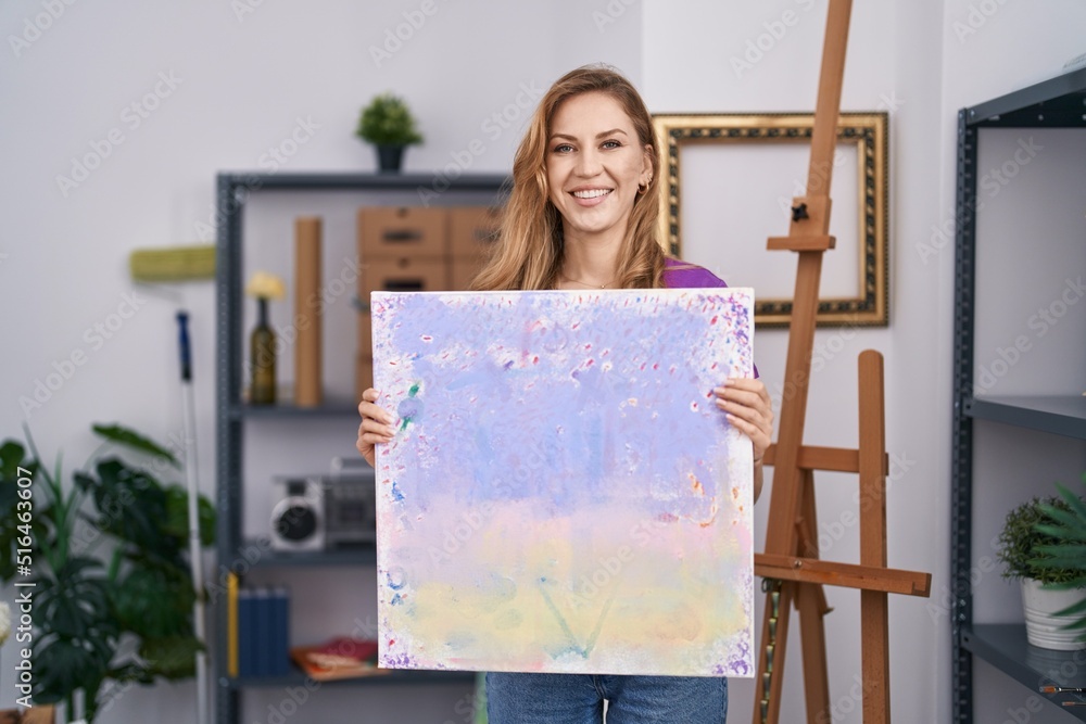 Sticker Beautiful blonde woman holding painting canvas smiling with a happy and cool smile on face. showing teeth.