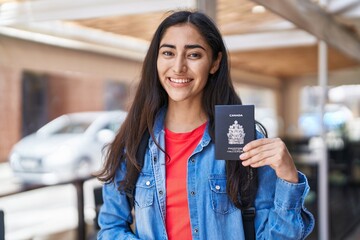 Young teenager girl holding canada passport looking positive and happy standing and smiling with a...