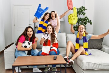 Group of young women watching and supporting soccer match at home.