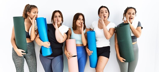 Fototapeta na wymiar Group of women holding yoga mat standing over isolated background hand on mouth telling secret rumor, whispering malicious talk conversation