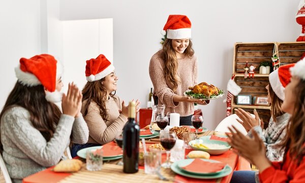 Group of hispanic women clapping and sitting on the table. Woman standing and holding roasted turkey celebrating Christmas at home.