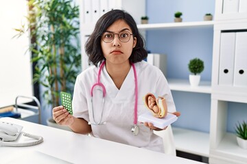 Young hispanic doctor woman holding anatomical model of uterus with fetus and birth control pills...