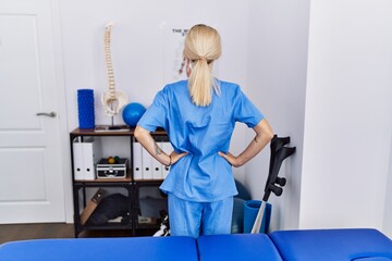 Young physiotherapist woman working at pain recovery clinic standing backwards looking away with arms on body