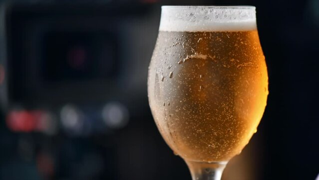 Close view of a glass of cold beer with bubbles and foam, walking people on the background