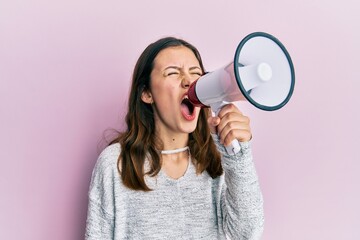 Young brunette woman shouting and screaming through megaphone over pink isolated background