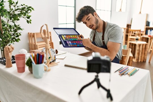 Young hispanic artist man smiling happy making online paint class at art studio.