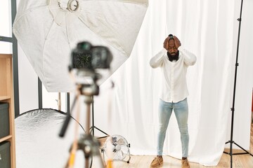 African american man posing as model at photography studio suffering from headache desperate and stressed because pain and migraine. hands on head.