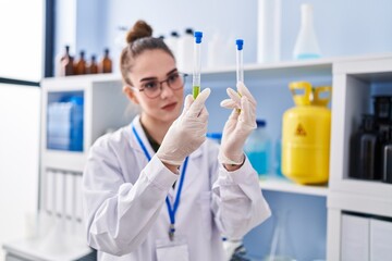 Young woman scientist smiling confident holding test tubes at laboratory