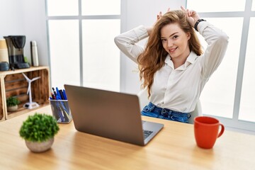 Young caucasian woman working at the office using computer laptop posing funny and crazy with...
