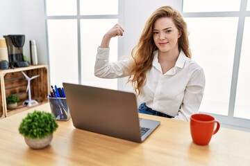 Young caucasian woman working at the office using computer laptop strong person showing arm muscle,...