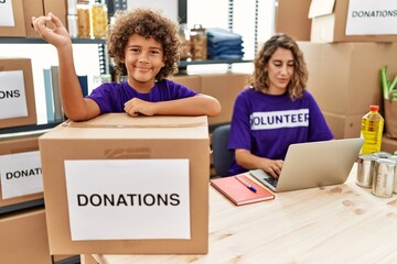 Young mother with little son wearing volunteer t shirt at donations stand smiling happy pointing with hand and finger to the side